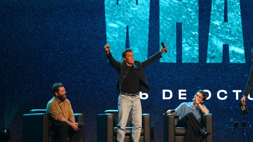Josh Brolin de pie en el escenario del panel de Whalefall con los brazos en alto